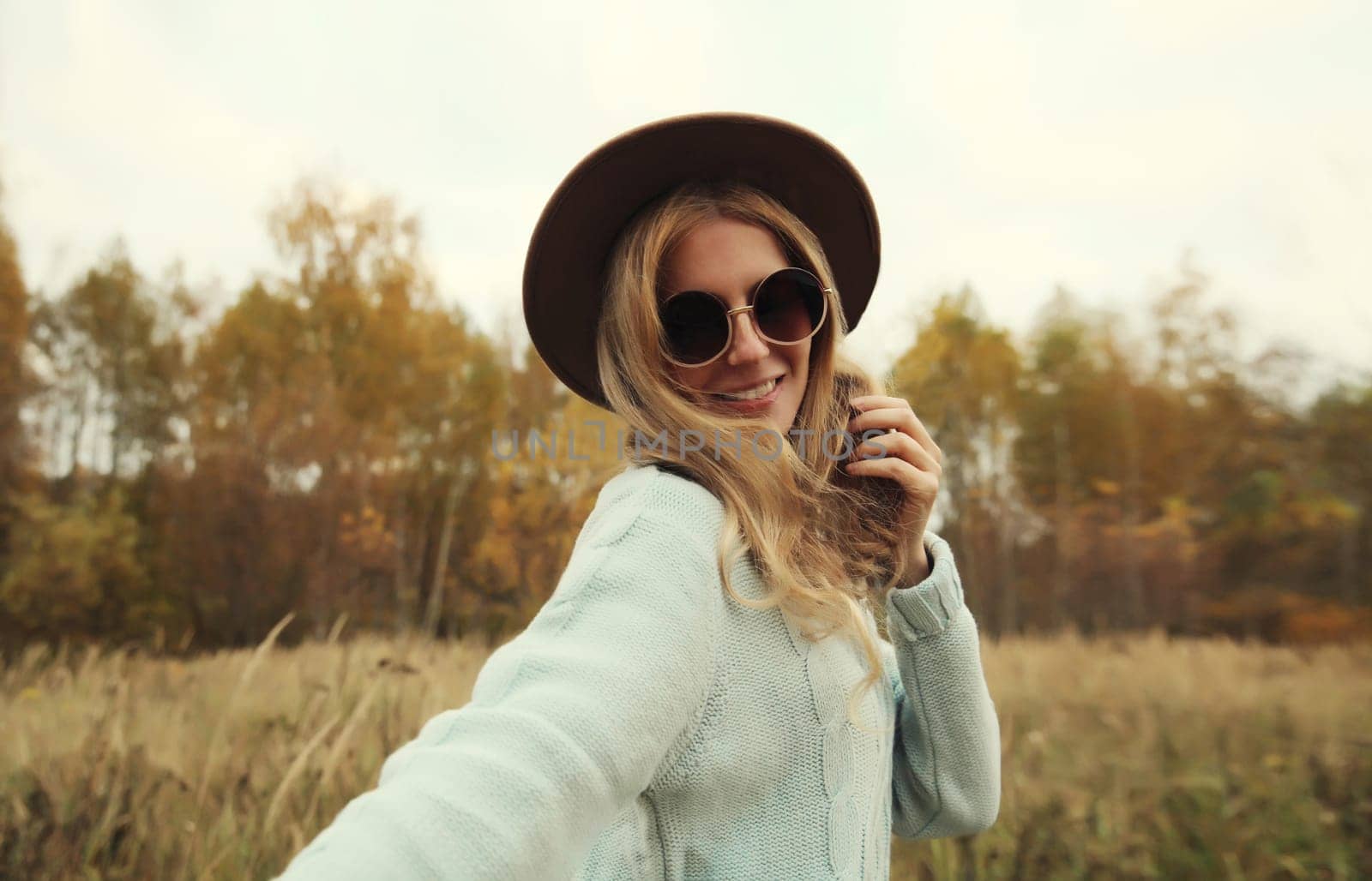 Autumn portrait of stylish modern happy young woman having fun and dancing, fashionable girl smiling in hat, sweater outdoors in park, warm fall season