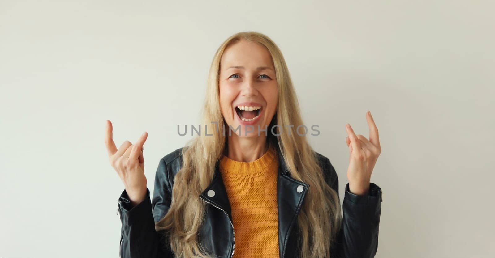 Portrait of happy stylish emotional mature woman overjoyed with crazy expression doing rock symbol with hands up, fashionable middle aged female having fun on white studio background