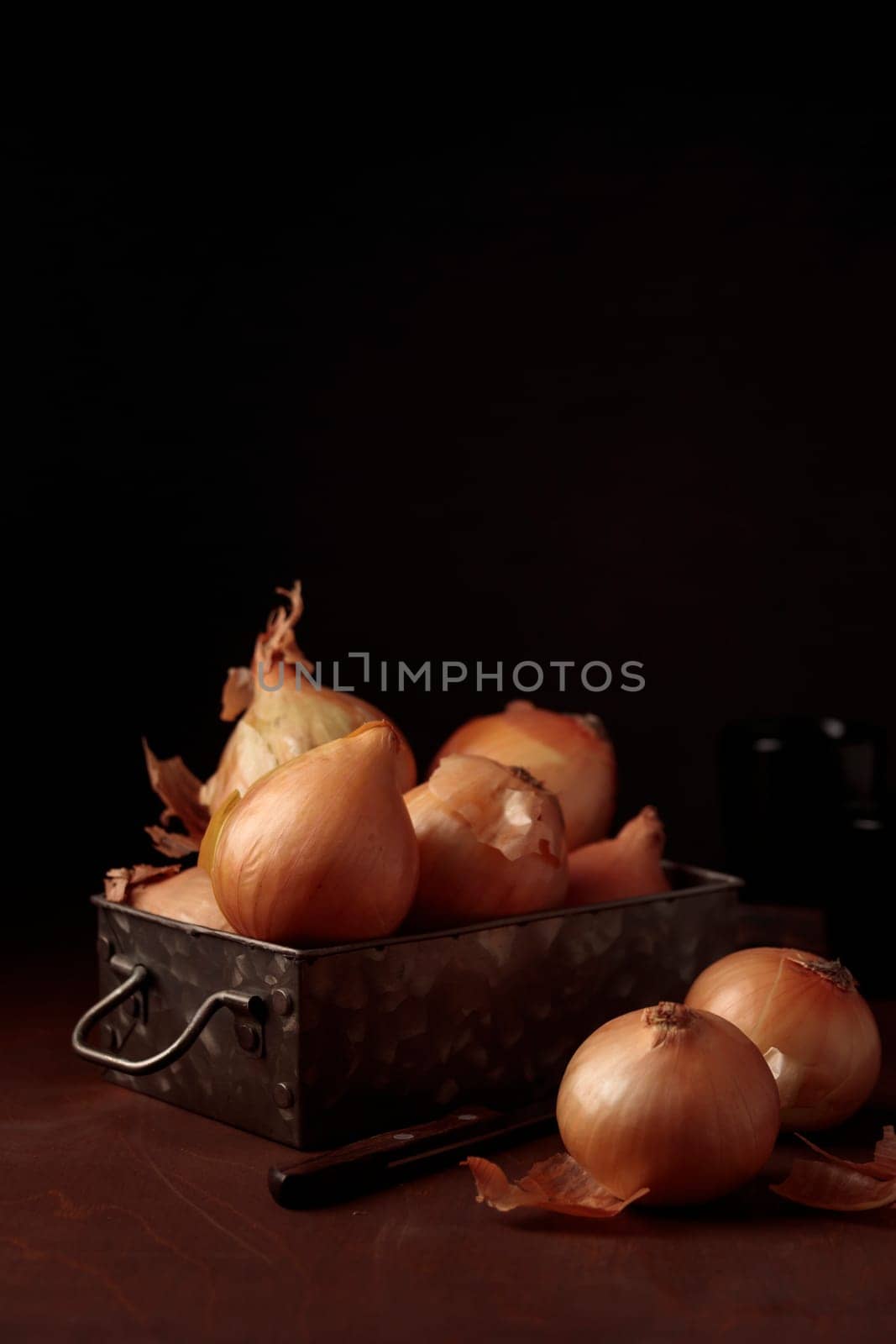 Fresh harvest yellow onion bulbs with peel in a vintage metal box on a table on a dark background, organic product for healthy food, ingredient for home cooking dishes, vertical close-up banner with a copy space