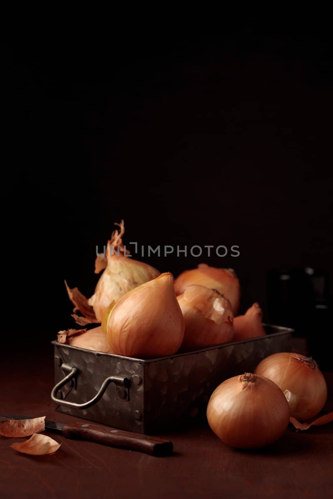 Fresh harvest yellow onion bulbs with peel in a vintage metal box on a table on a dark background, organic product for healthy food, ingredient for home cooking dishes, vertical close-up banner with a copy space