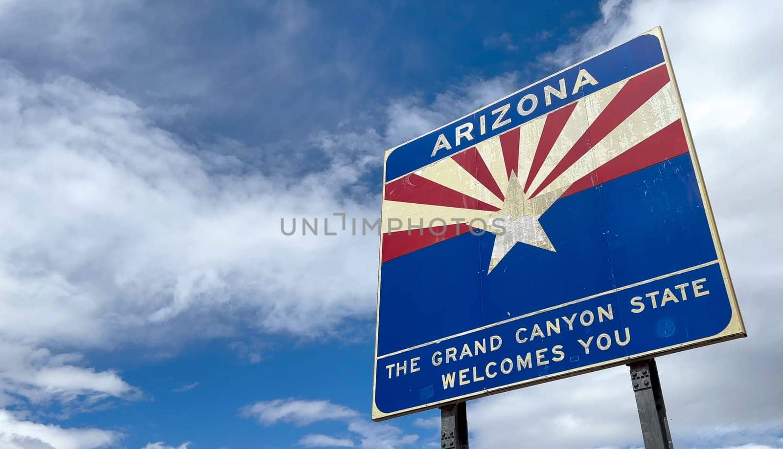 A bright and sunny view of an Arizona welcome sign against a beautiful blue sky with fluffy white clouds. Perfect for showcasing travel, tourism, and the beauty of the American Southwest - USA