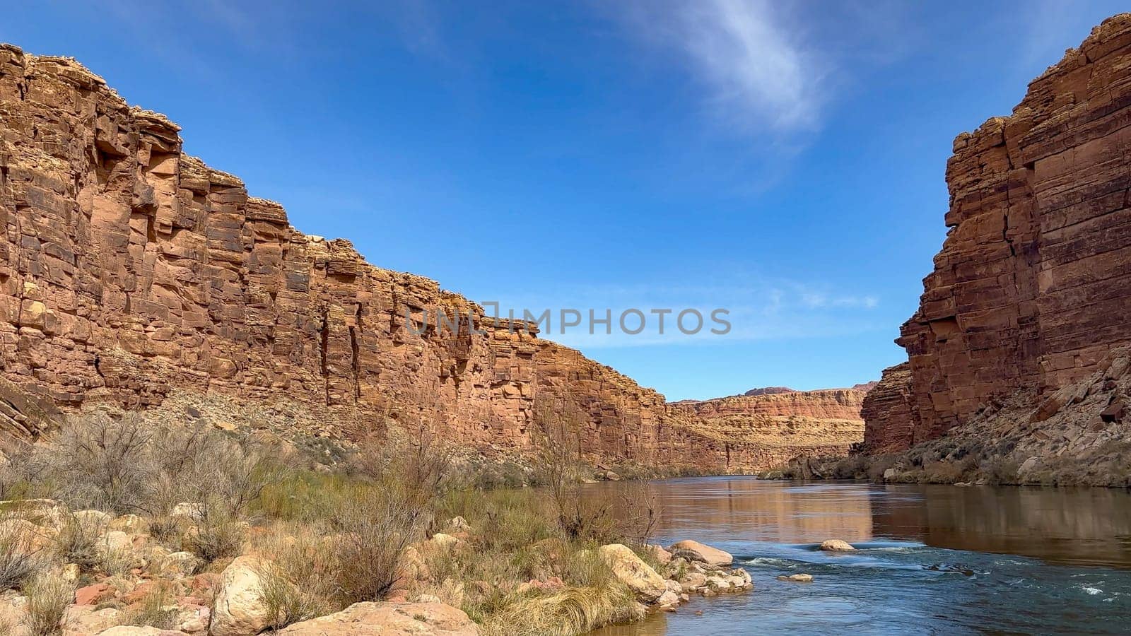 Scenic view of the Colorado River flowing through Marble Canyon in Arizona on a sunny day with blue skies. The canyon has steep red rock cliffs on either side. Taken at river level - USA