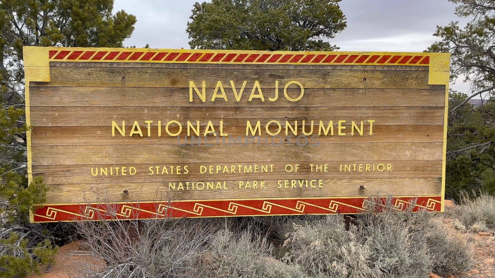 Kayenta, Arizona, USA - 03.12.2024: Navajo National Monument wooden entrance sign, with trees and desert landscape. Tourism, travel destinations, Native American history and culture.