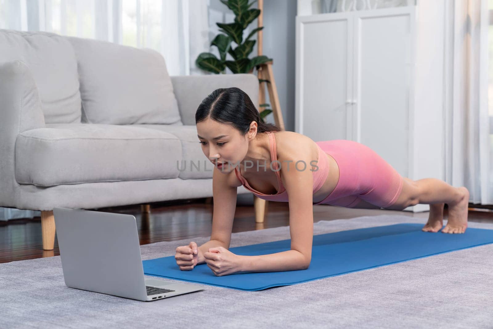 Fit young asian woman planing on the living room floor while following exercise instruction on online training video. Healthy lifestyle workout routine at home. Balance and endurance concept. Vigorous