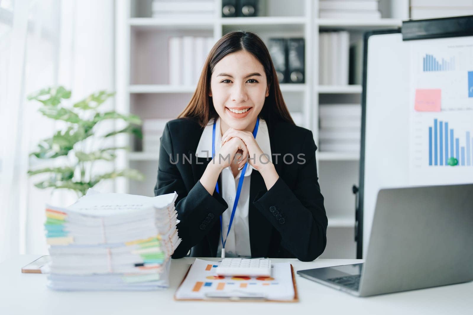 Portrait of a woman business owner showing a happy smiling face as he has successfully invested her business using computers and financial budget documents at work.