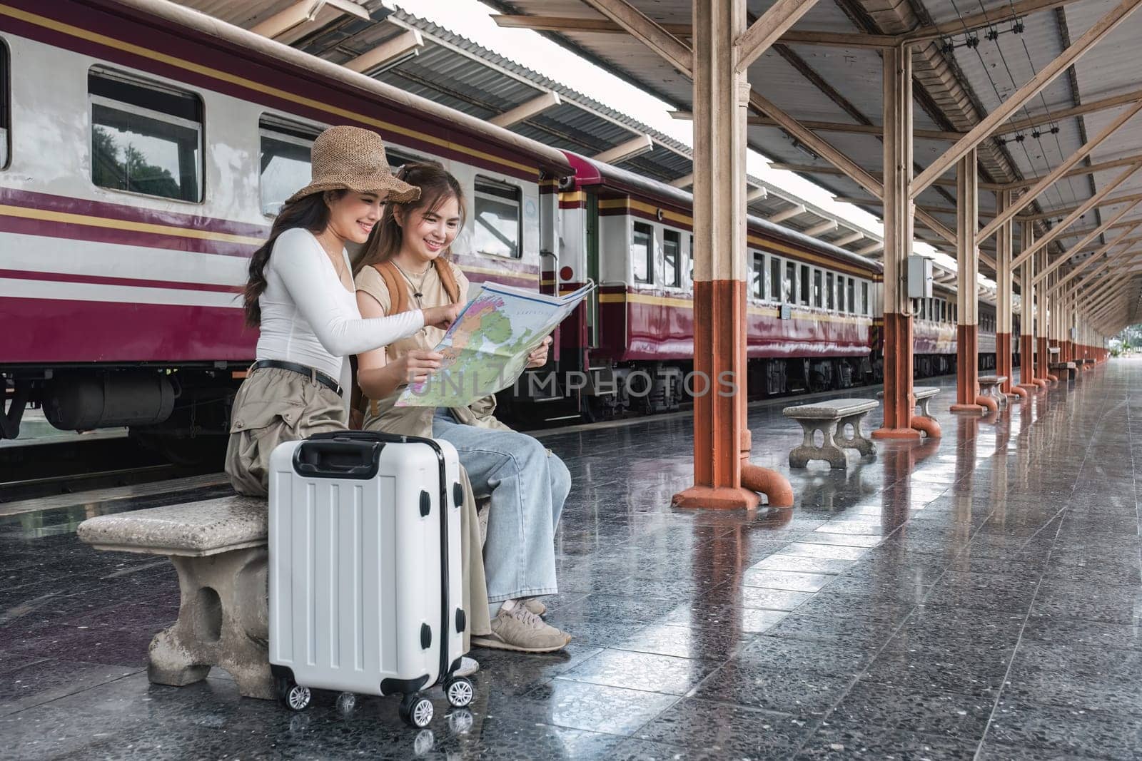 Two women look at tourist maps while waiting to travel at the train station..