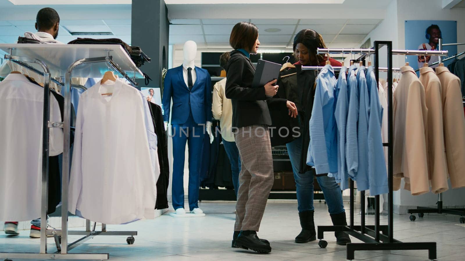 Young employee helping woman to choose shirts by DCStudio