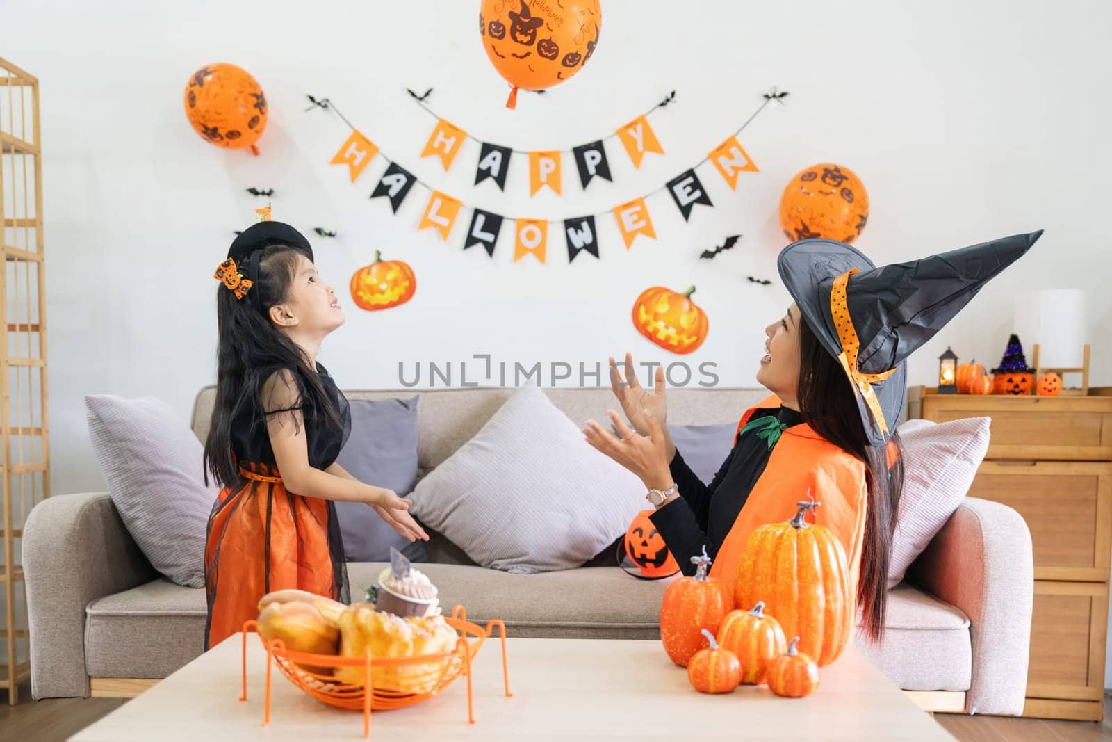 Happy family mother and child happy girl with Halloween at home together beautifully decorated. pretending to release air from a balloon at a child girl by nateemee