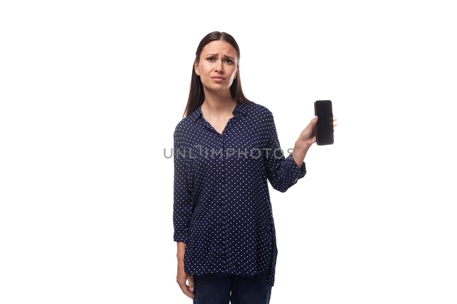 young cheerful cute caucasian brunette lady dressed in dark blue blouse holding smartphone with mockup.