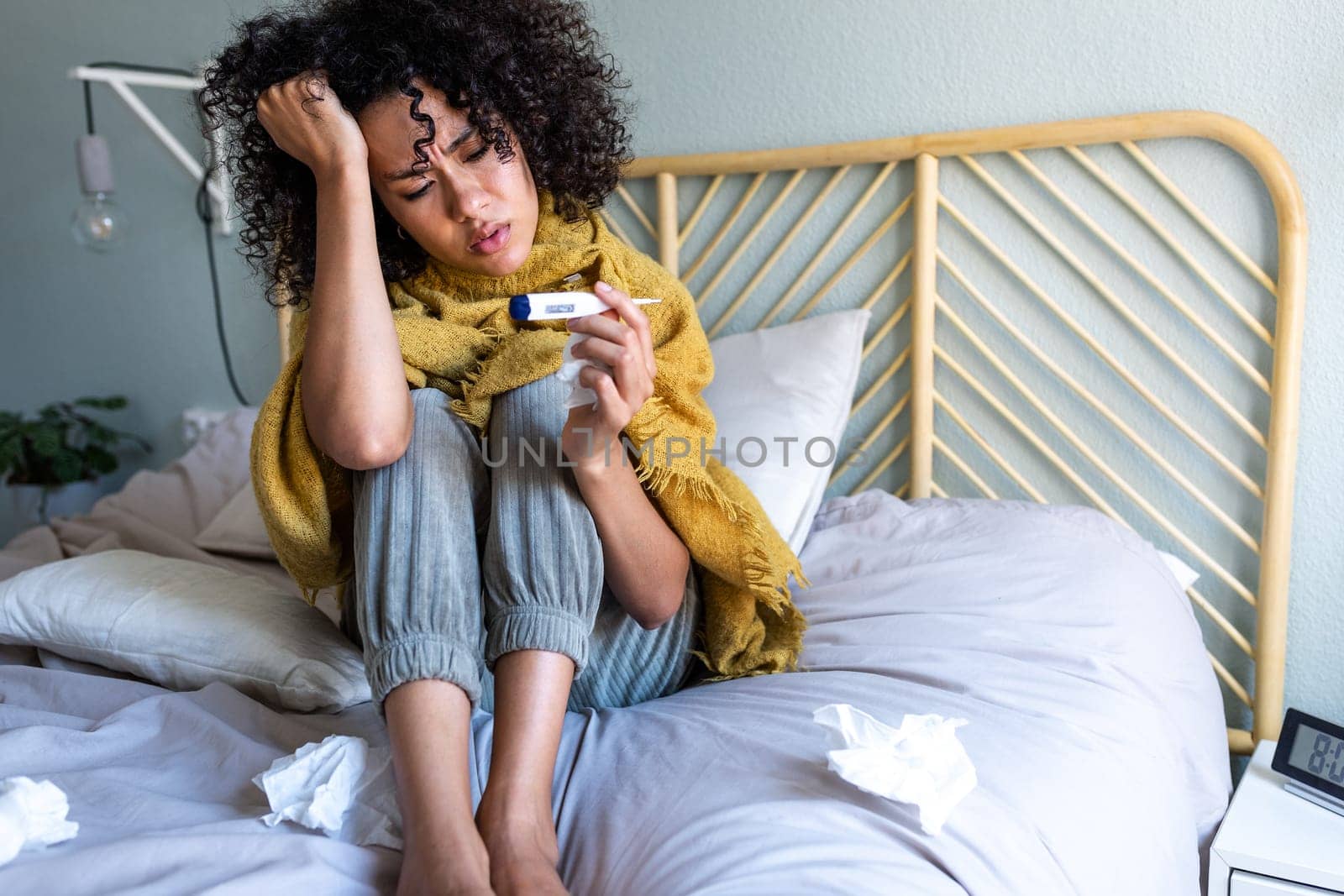 African American young woman checking temperature with thermometer, sitting in bed feeling unwell. Woman sick in bed. Sickness concept.
