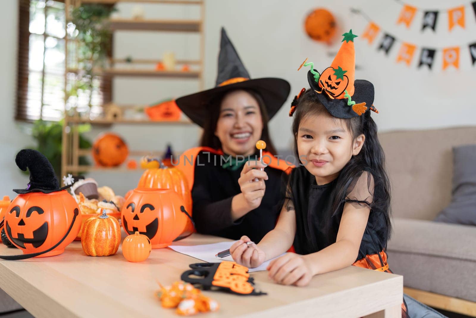 Asian mom and cute daughter celebrate Halloween and balloon pumpkin together at home. Halloween activity concept.