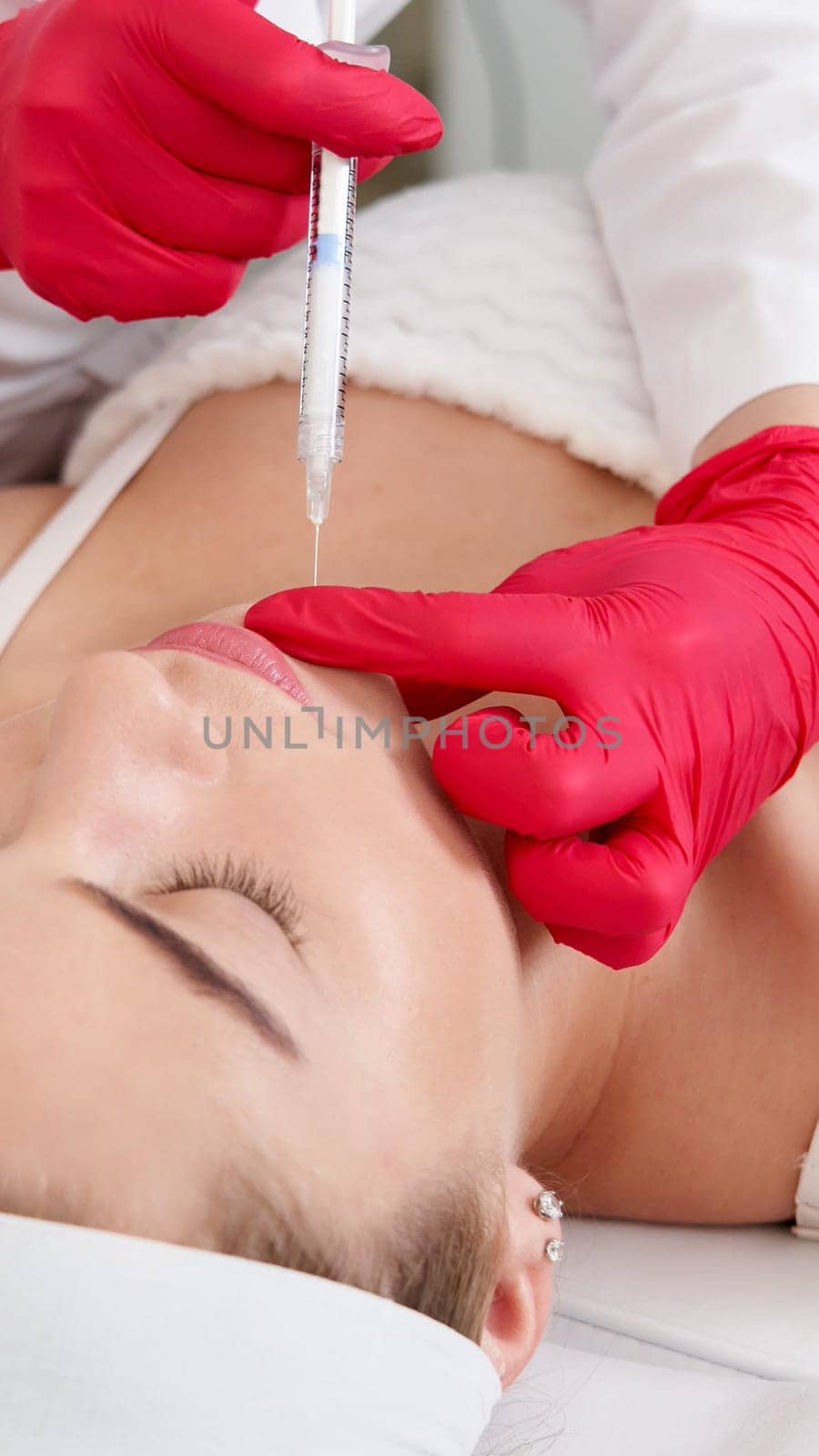 Beautician making injection in the chin with syringe in beauty salon. Cosmetic rejuvenating facial treatment