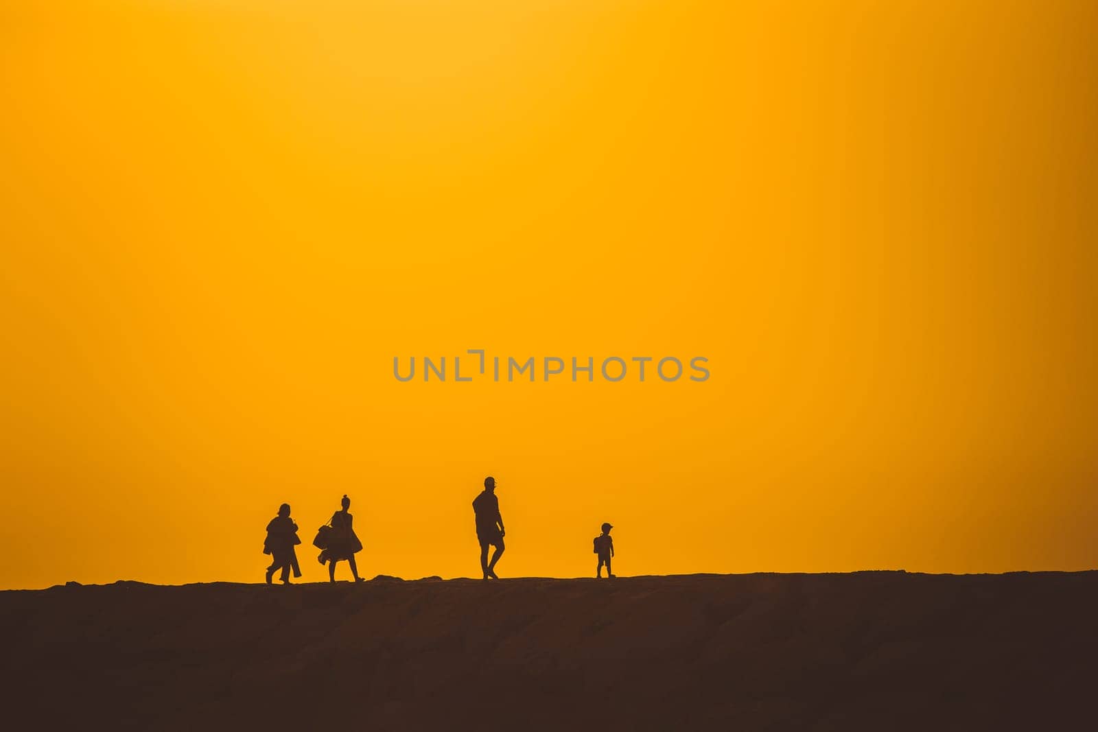 Silhouettes of people walking on a hill at a bright sunset. Mid shot