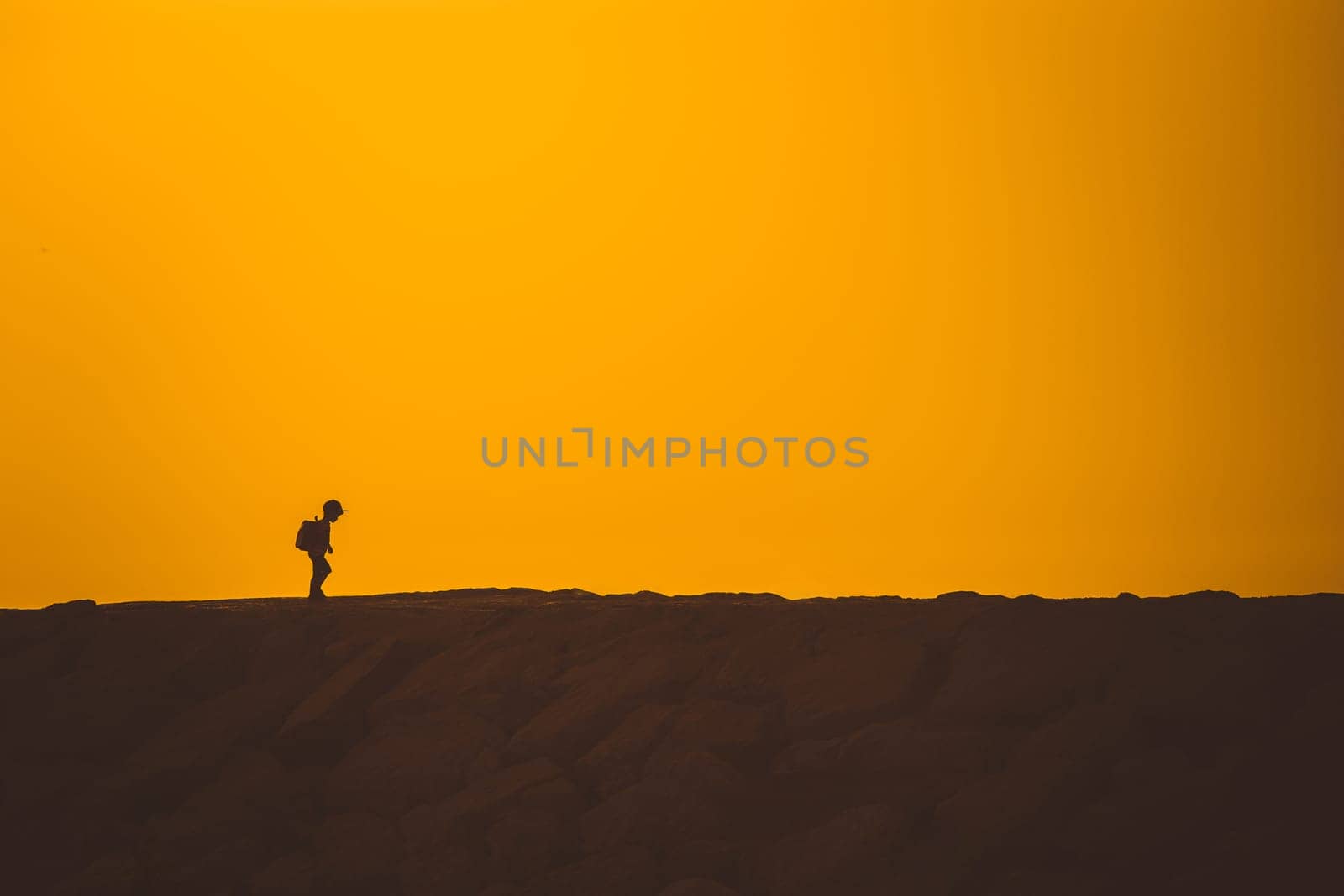 A little boy standing on the hill at sunset. Mid shot