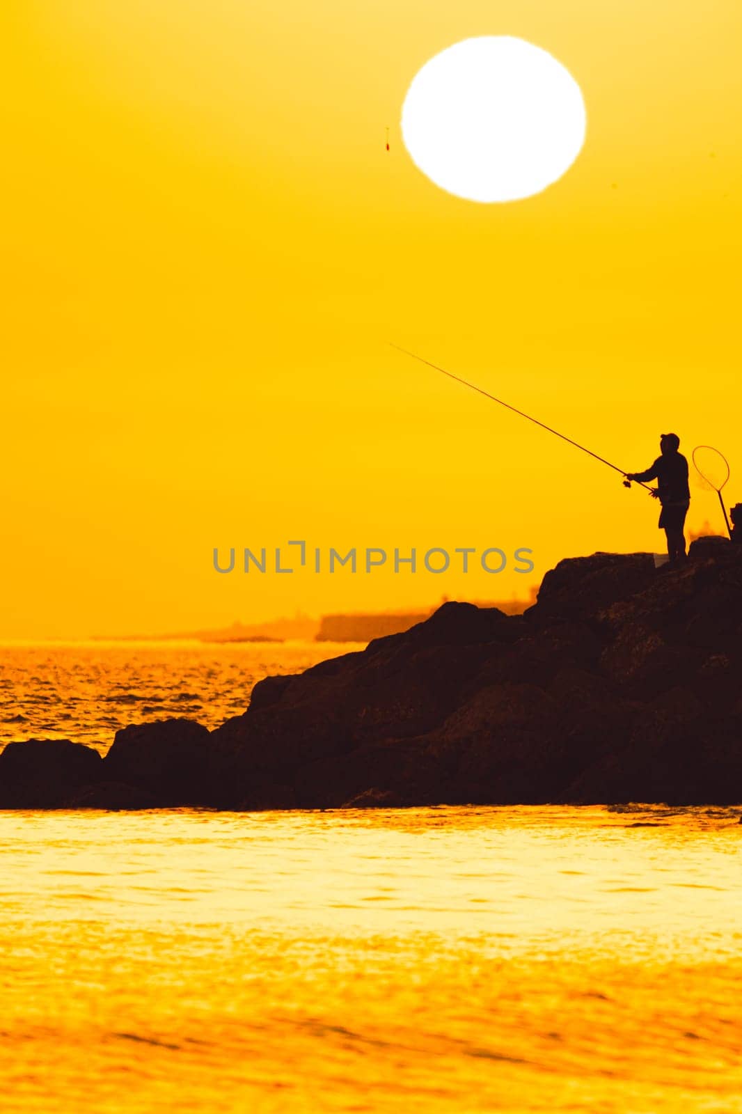 Silhouette of a man fishing at sunset. Vertical shot