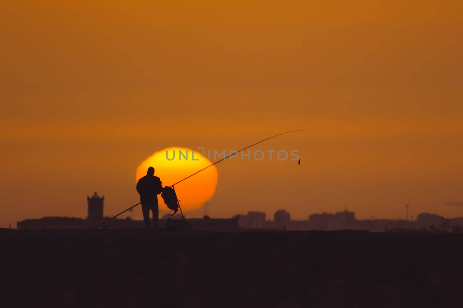 A man is fishing at sunset standing on the hill. Mid shot