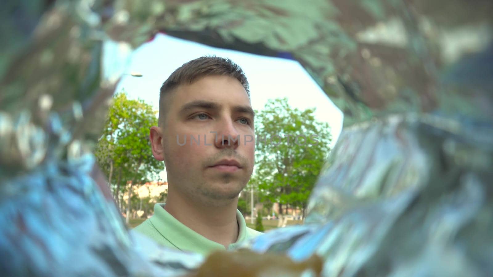 A young man eats potato chips from a packet while walking in the park. View of a man from a bag of chips. 4k