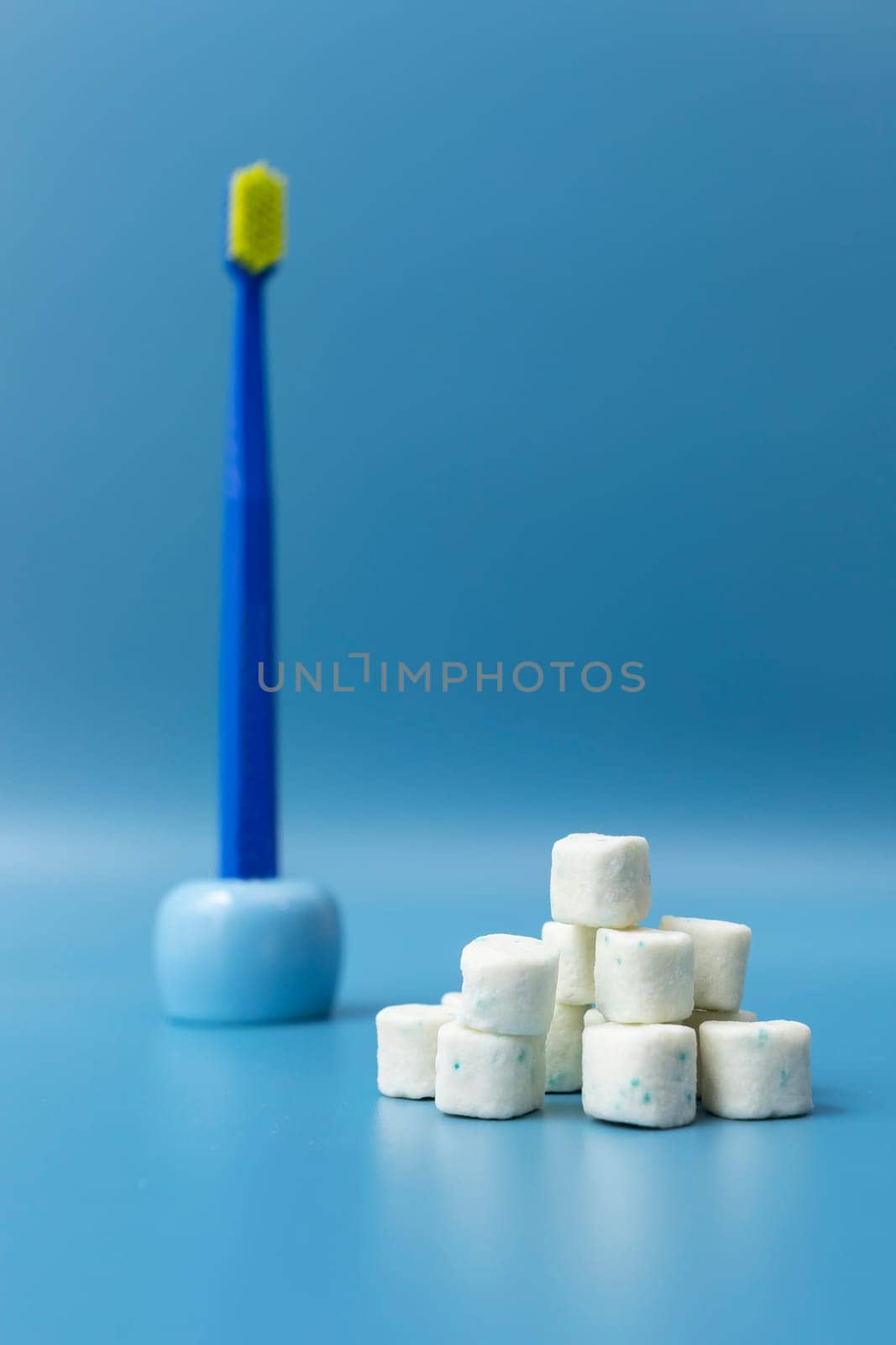 Heap Of Healthy Sugar-Free Xylitol Cubes Of White Chewing Gum, Toothbrush on Blue Background. Healthy Teeth, Beautiful Smile Concept. Top View, Copy Space. Bubble Gum, Oral Hygiene. Vertical Plane. by netatsi