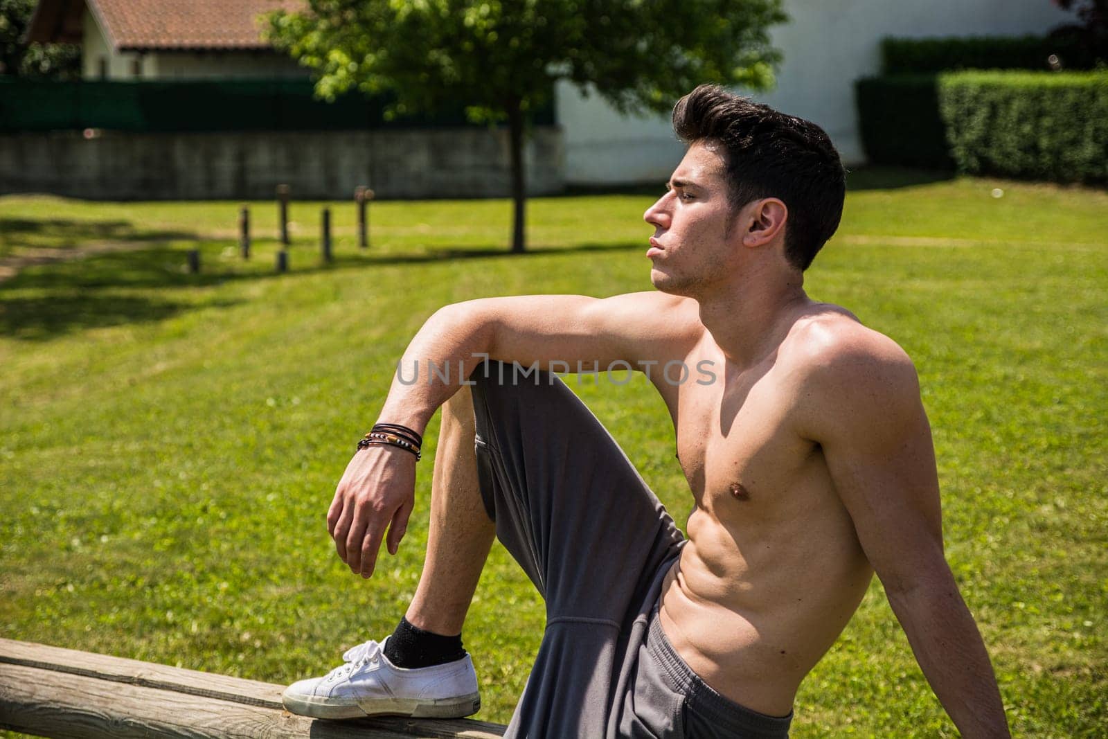 A shirtless man sitting on a bench in a park. Photo of a man enjoying a peaceful moment on a park bench