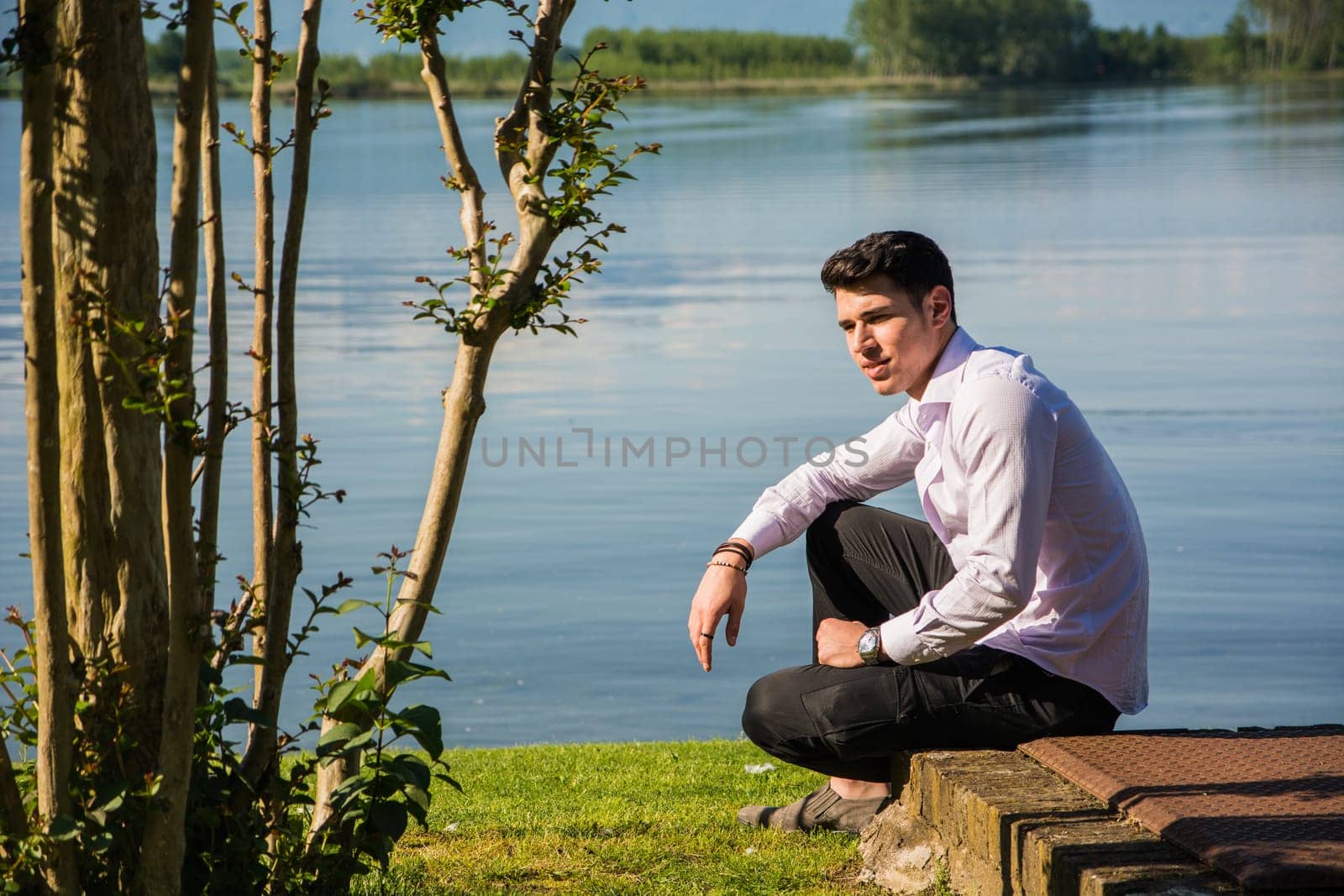 A man sitting on a bench next to a body of water. Photo of a man sitting on a bench by the water's edge