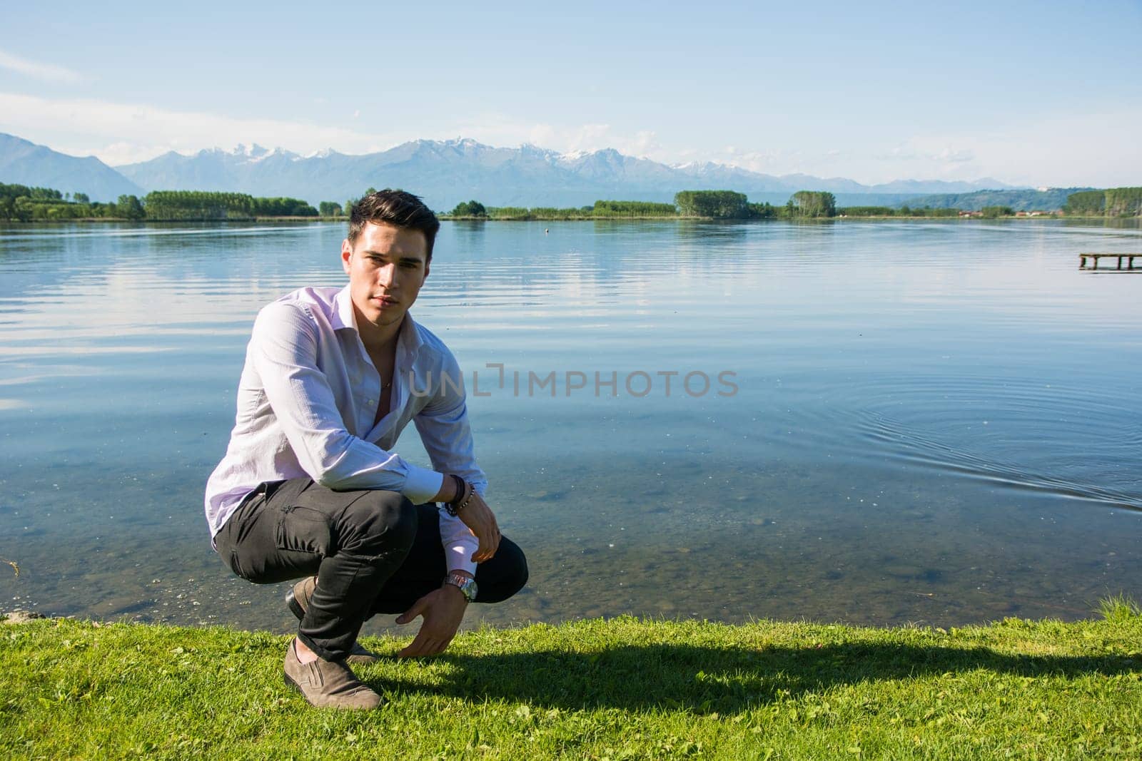 A young attractive man kneeling down next to a body of water. Photo of a man kneeling by the water's edge