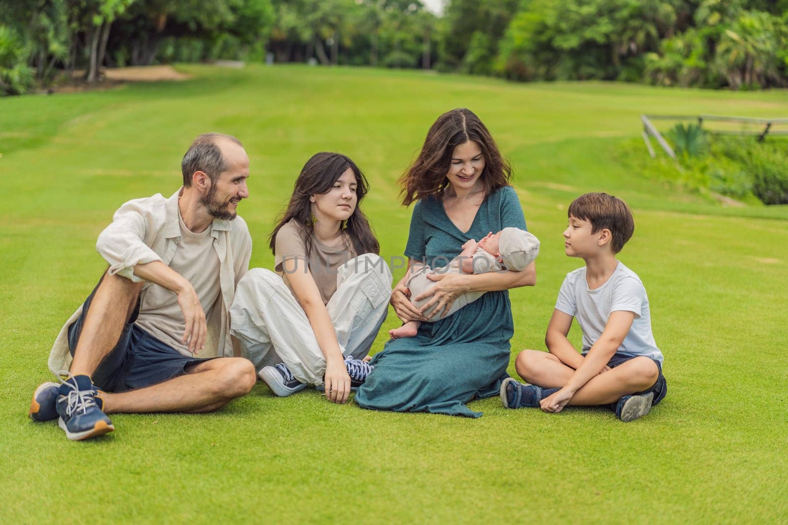 Happy couple in their 40s, surrounded by adult children, cradle a newborn in a sunlit park. Love, family, and generations in harmony by galitskaya