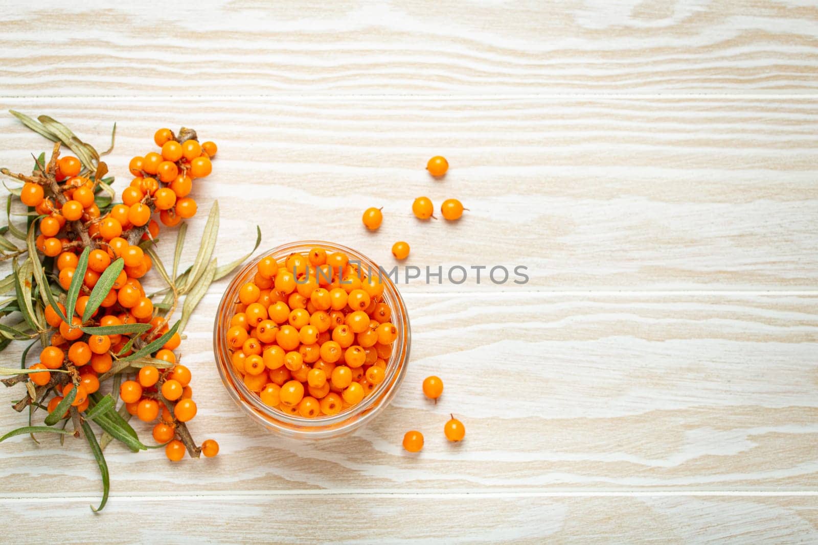 Sea buckthorn ripe berries in glass jar and branches with leaves top view on white wooden rustic background, great for skin, heart, vessels and immune system. by its_al_dente