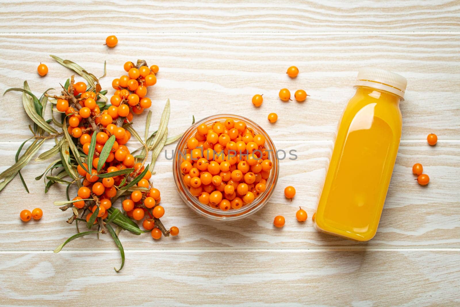 Sea buckthorn healthy drink in bottle, ripe berries in glass jar and branches with leaves top view on white wooden rustic background, great for skin, heart, vessels and immune system..
