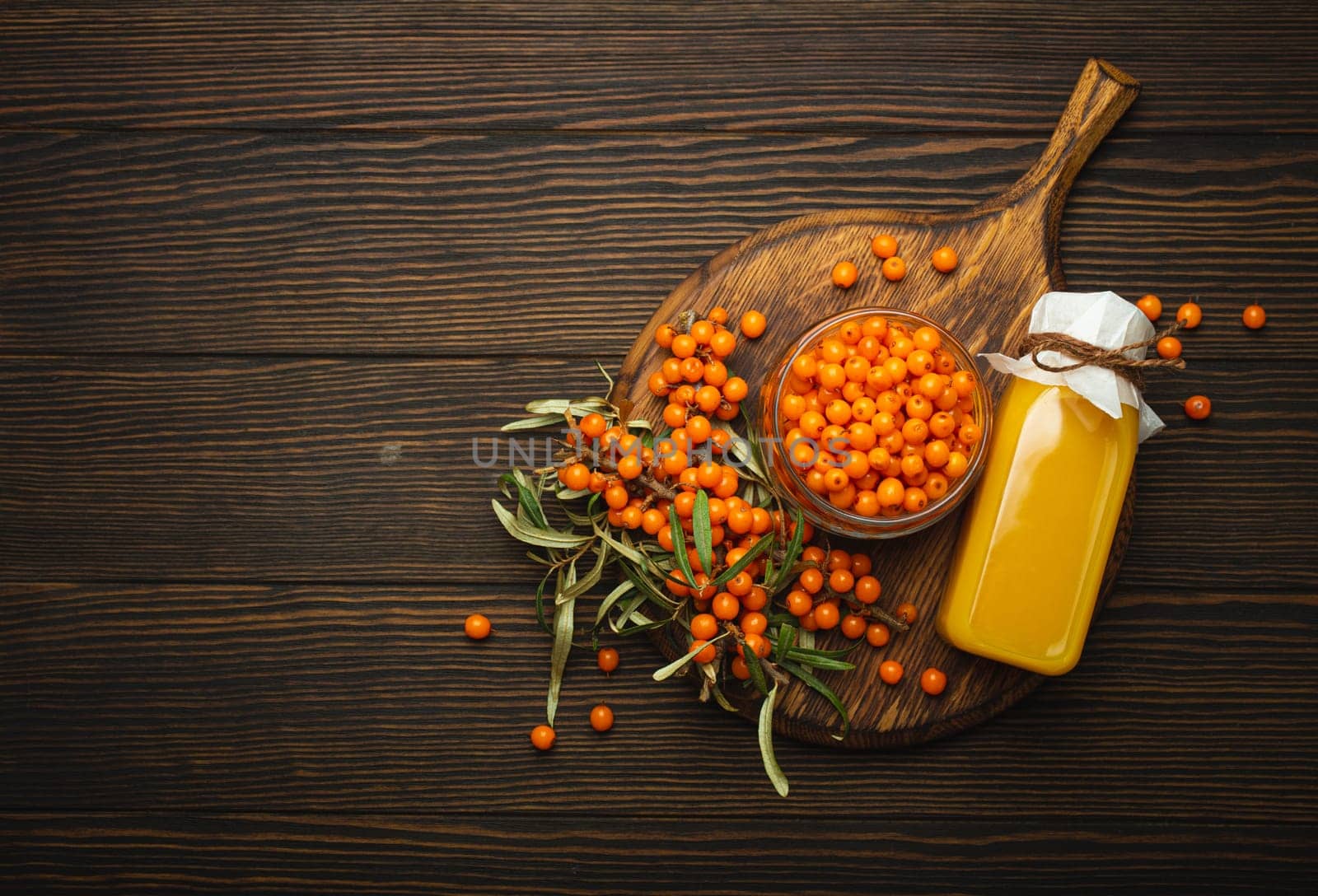 Sea buckthorn healthy drink in bottle, ripe berries in glass jar and branches with leaves top view on dark wooden rustic background, great for skin, heart, vessels and immune system. Copy space. by its_al_dente