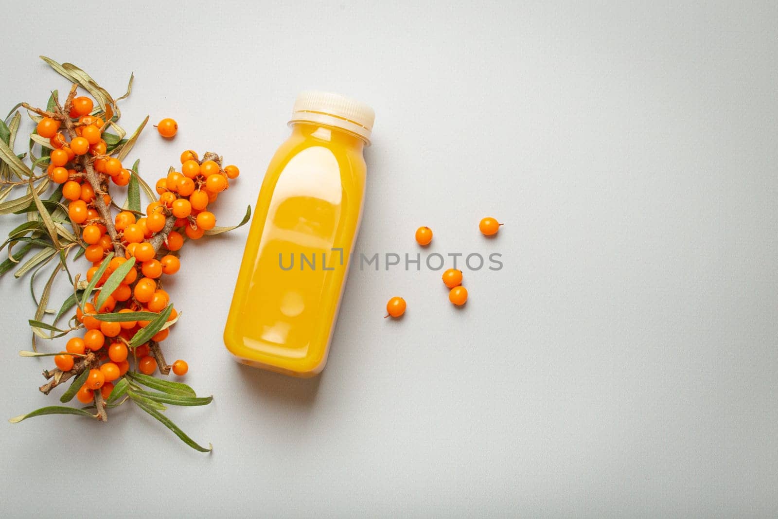 Sea buckthorn healthy juicy drink in bottle and branches with leaves and ripe berries top view on light grey simple background. Space for text. by its_al_dente