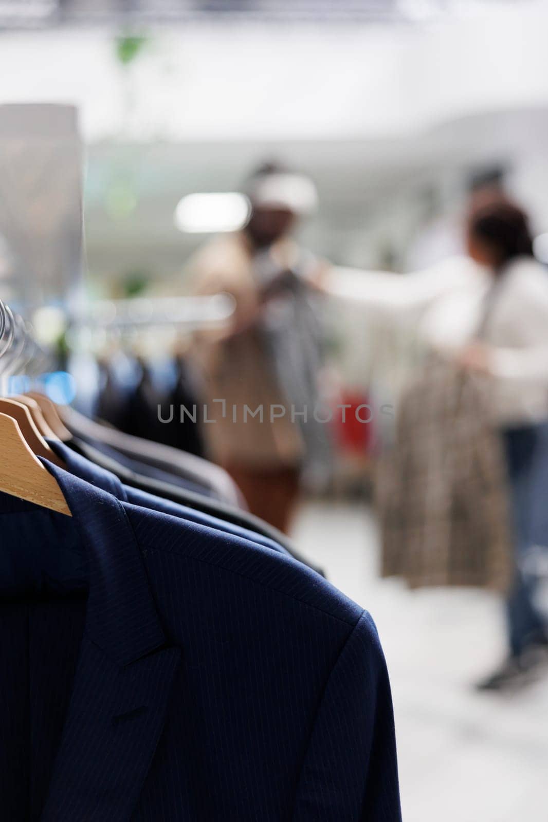 Trendy shirts hanging on rack in shopping mall with couple choosing clothes on blurred background. Casual menswear apparel on hangers in fashion boutique close up selective focus
