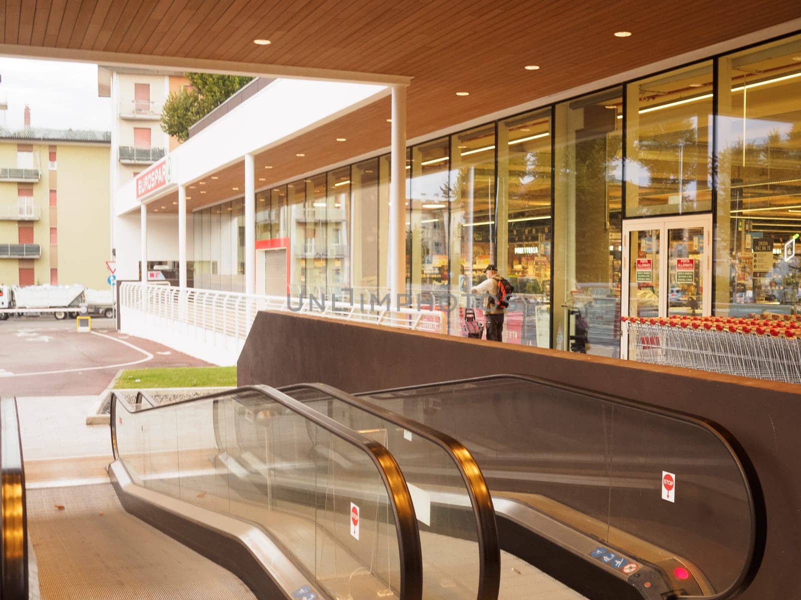 Cremona, Italy September 26th 2024 Modern supermarket with glass walls and escalators leading to the entrance with a customer entering