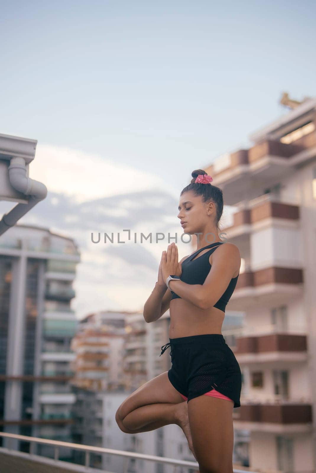 An individual who is highly focused is practicing yoga amidst a vibrant urban landscape as the sun sets