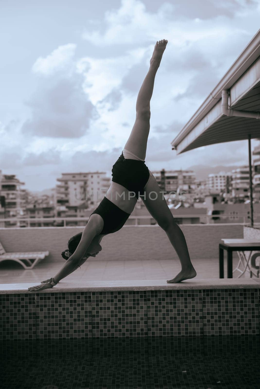 A woman elegantly performs a yoga pose on a rooftop, with a vast cityscape behind her, embodying strength