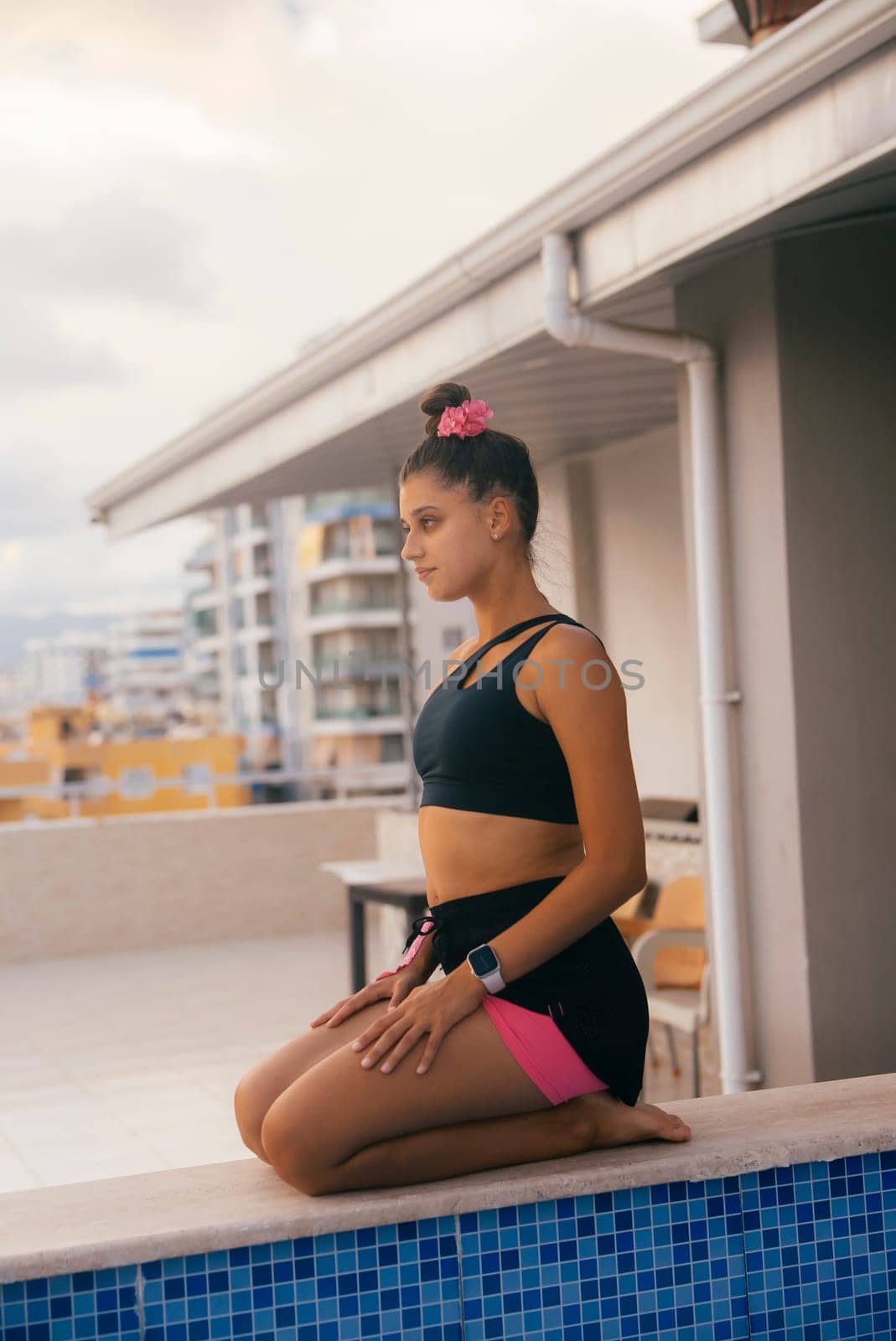A serene scene of a young woman in yoga pose at a rooftop pool, embracing tranquility and mindfulness.