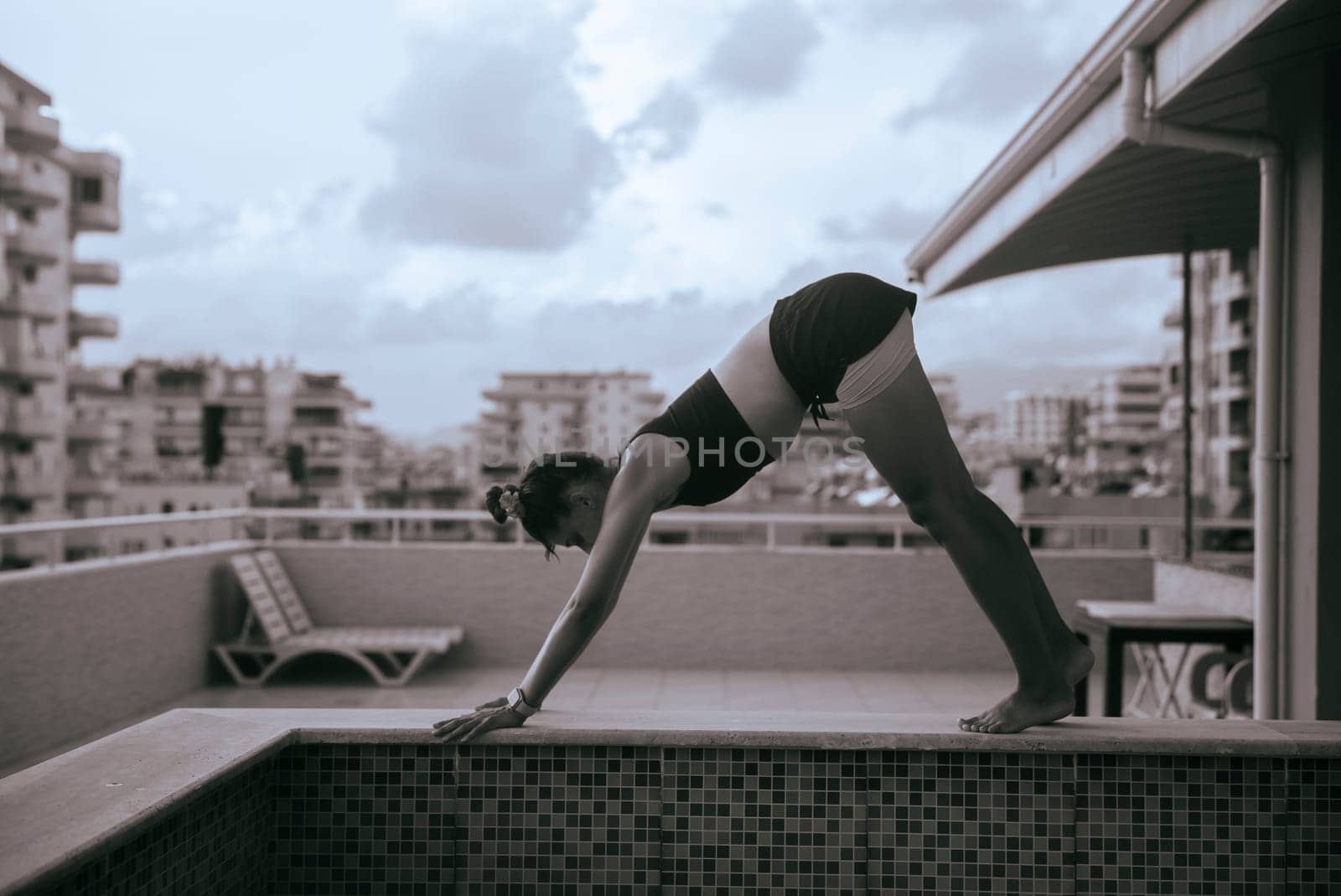 A woman skillfully practicing yoga in the downward dog position on a beautiful balcony overlooking the city