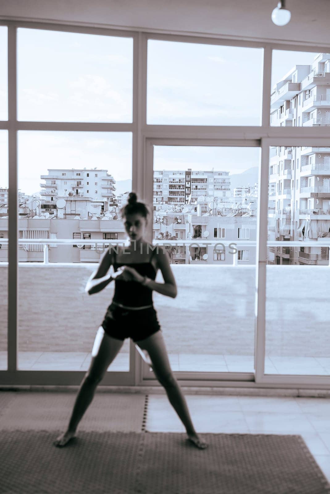 A focused young woman confidently strikes a challenging yoga pose in a bright, modern studio with stunning urban views