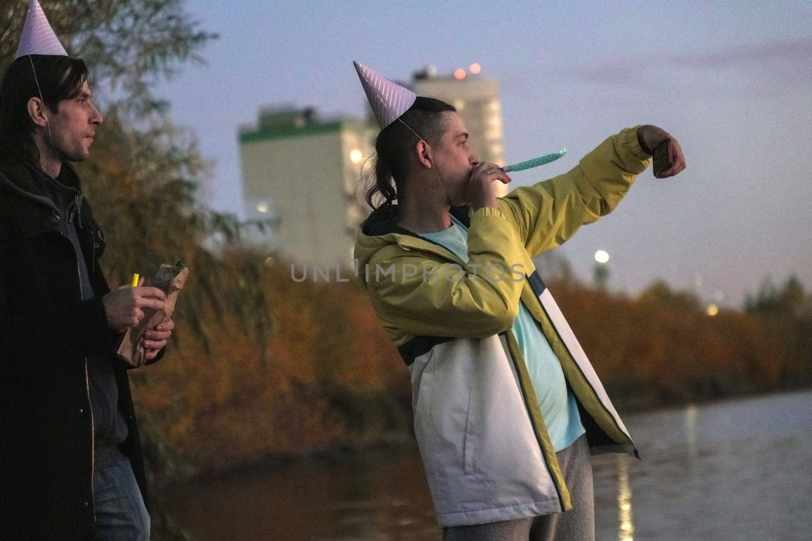 Celebrating friendship by the riverside at dusk with laughter, hats, and snacks during a joyful holiday gathering