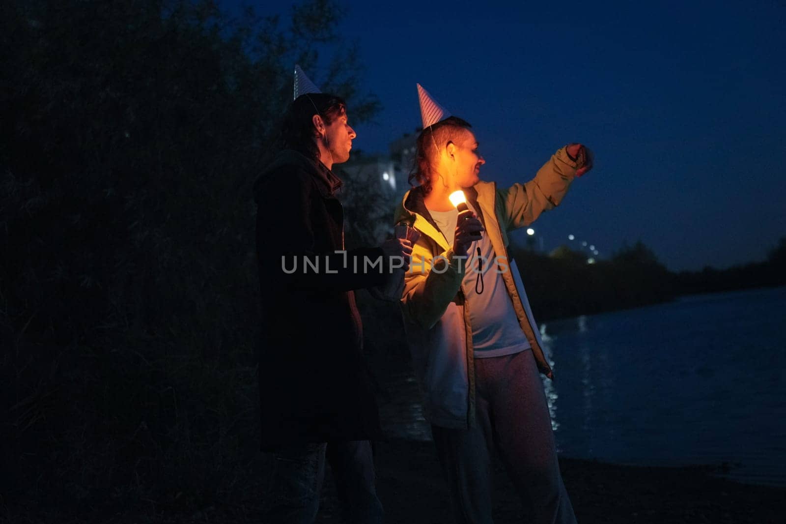 Two friends enjoy a memorable holiday evening by the water, laughing and sharing stories as they light the night with candles