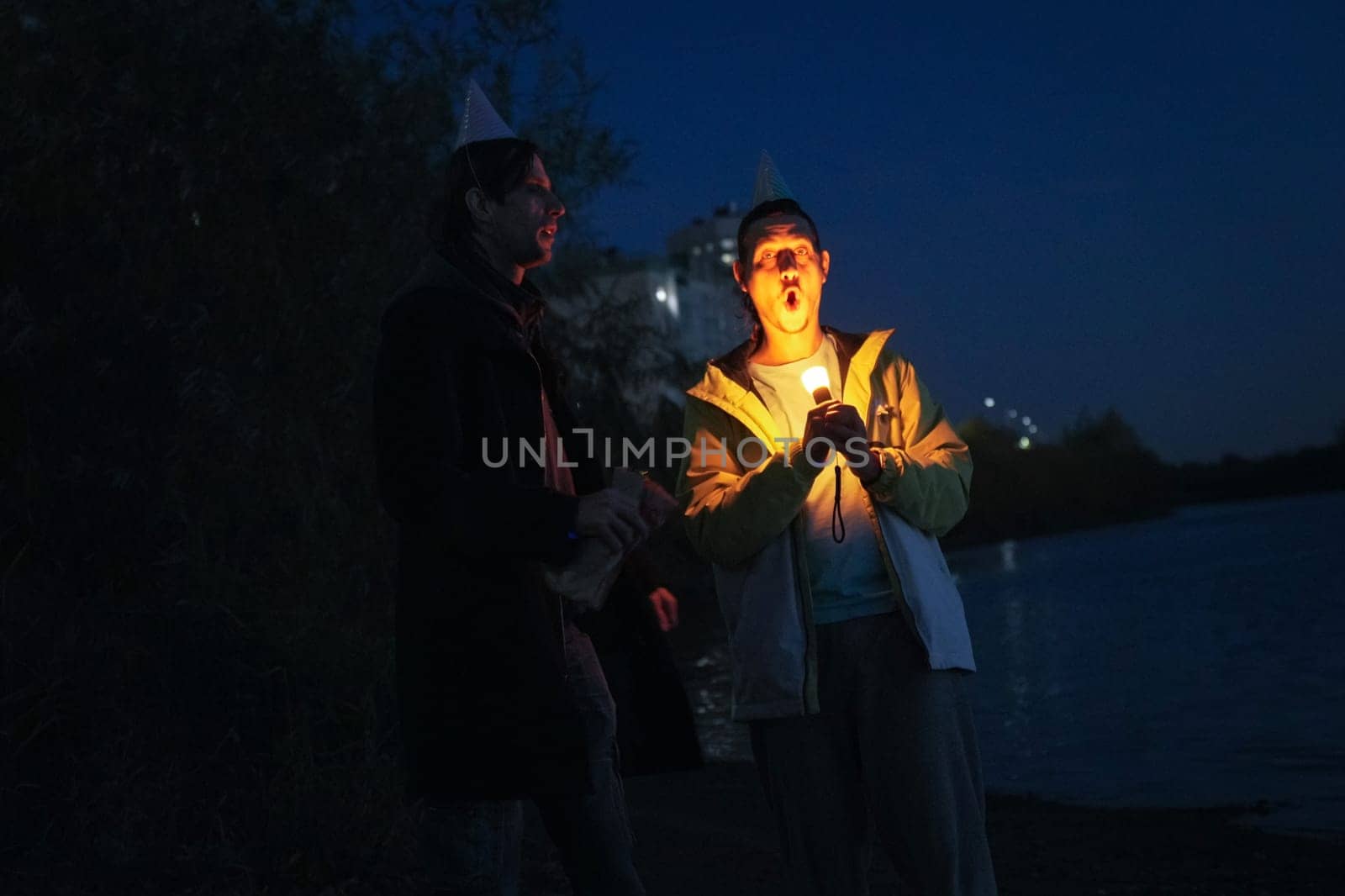 Friends celebrating a joyous holiday by the water, illuminated by candles and laughter under a starry night sky
