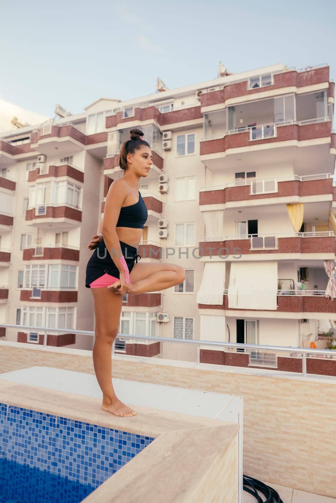 A woman actively engages in yoga practice near a serene pool area, showcasing a vibrant fitness and wellness lifestyle
