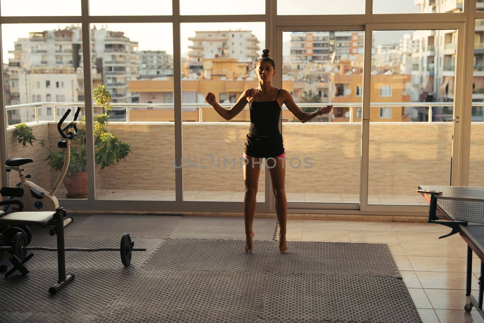 A woman performs a dynamic home workout, enjoying a beautiful urban view and embracing a healthy lifestyle
