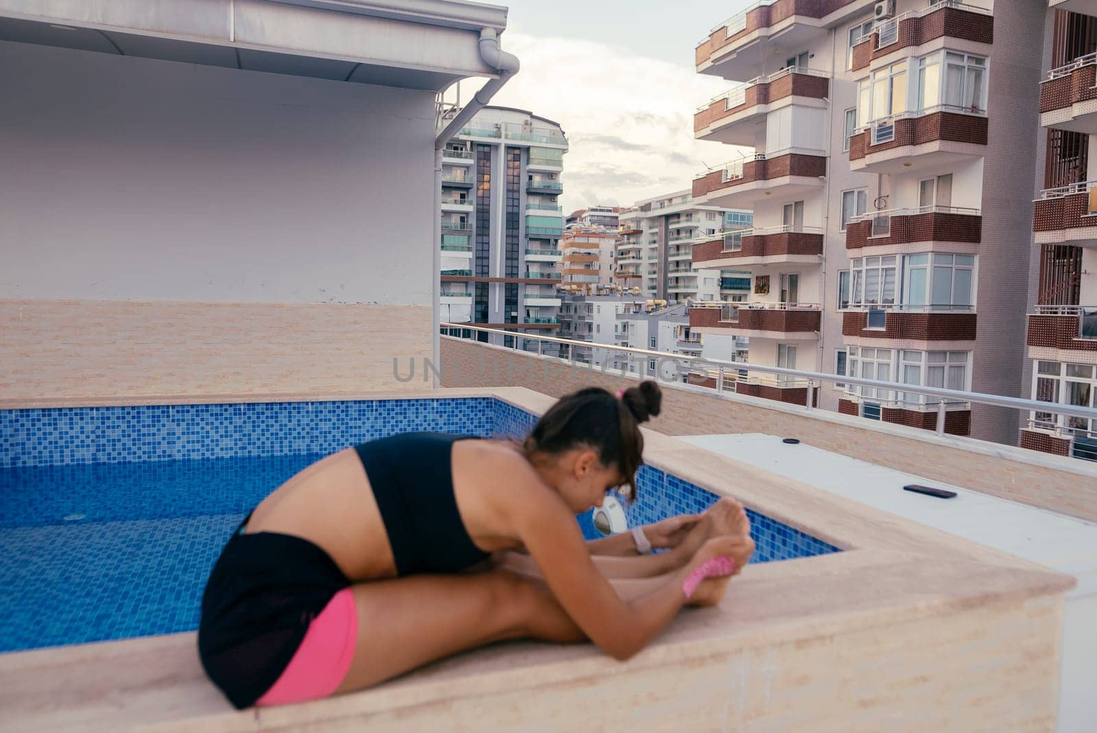 A person is actively engaged in yoga stretching beside a pool, with modern buildings elegantly rising in the background