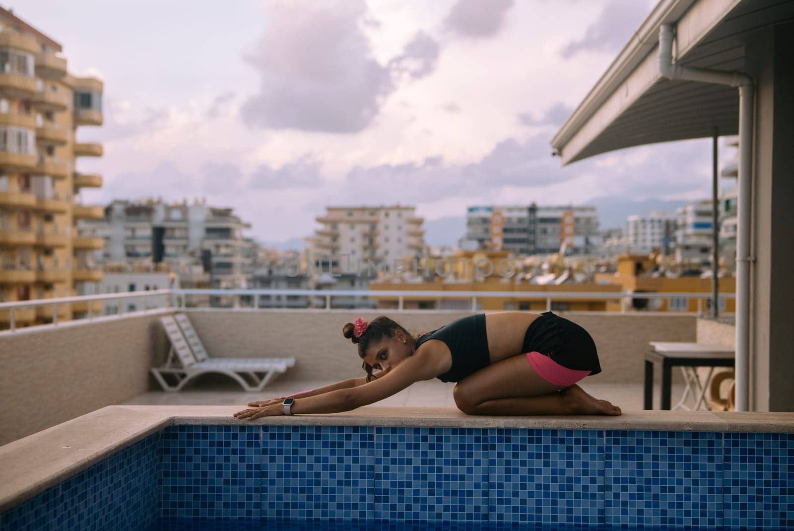 A person stretches skillfully by a pool, blending yoga practice with urban living in a serene setting