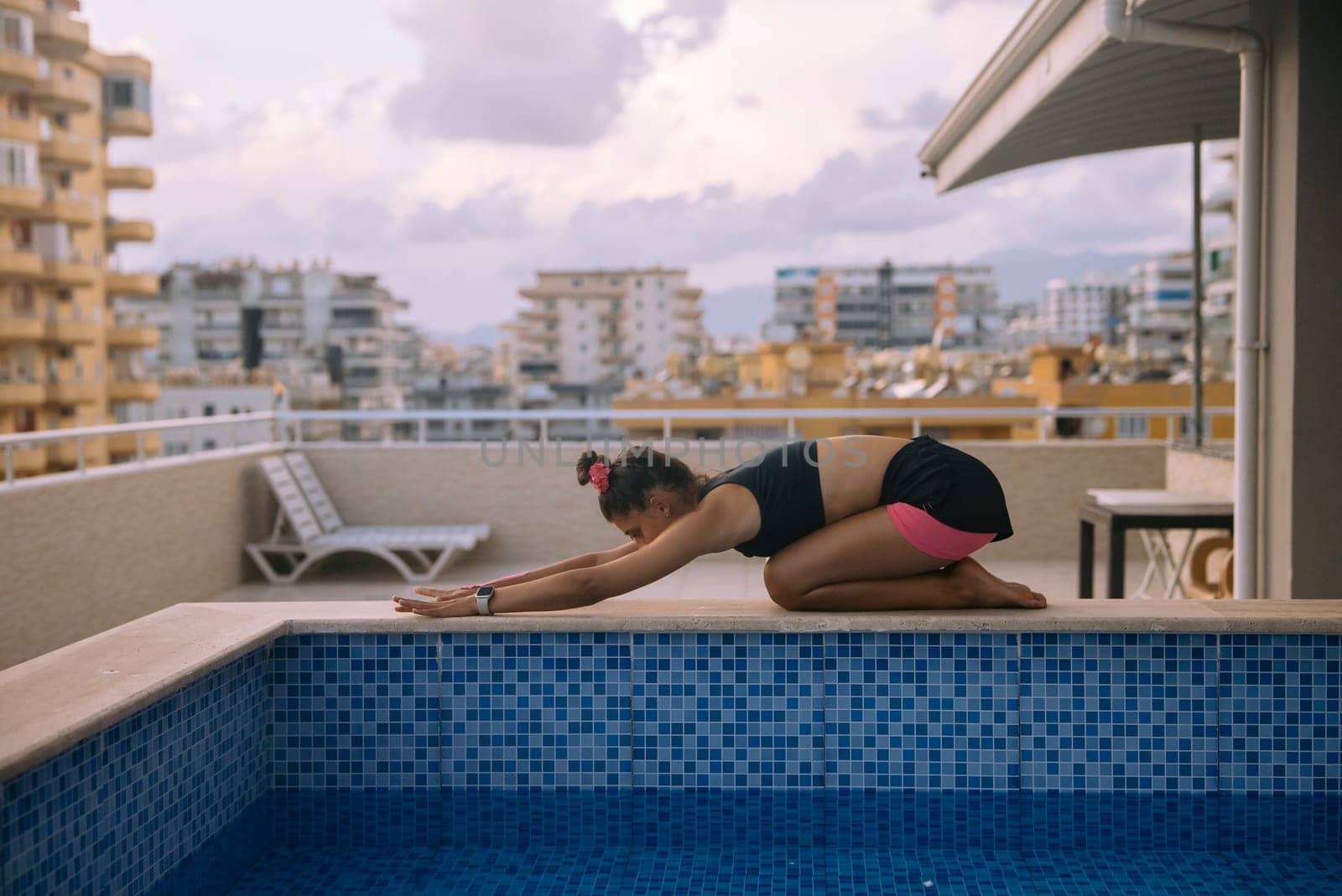A woman performs a tranquil yoga pose by a serene pool in a busy urban area, showcasing her fitness and peace