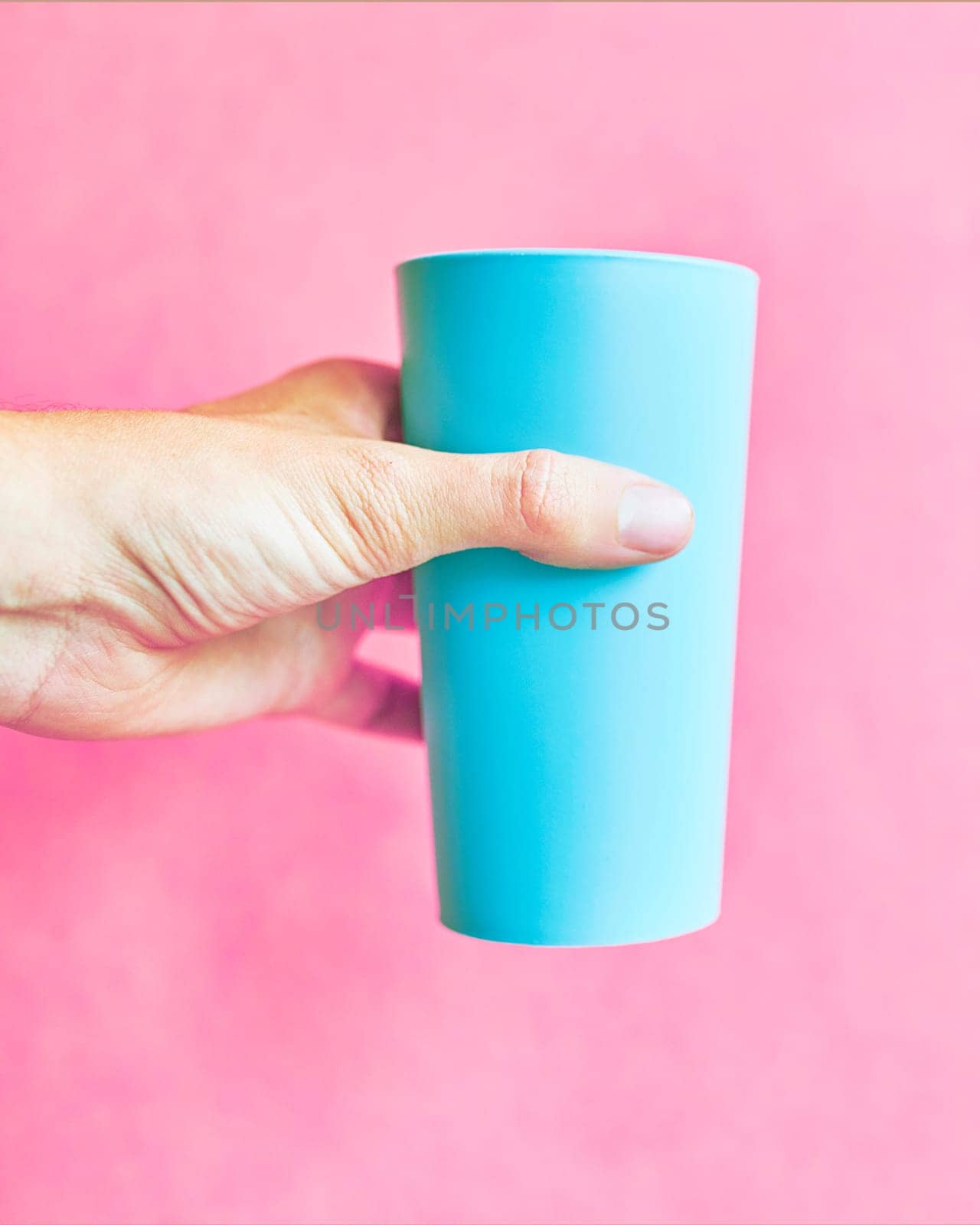 Man holds Colorful blue plastic cup on pink background.