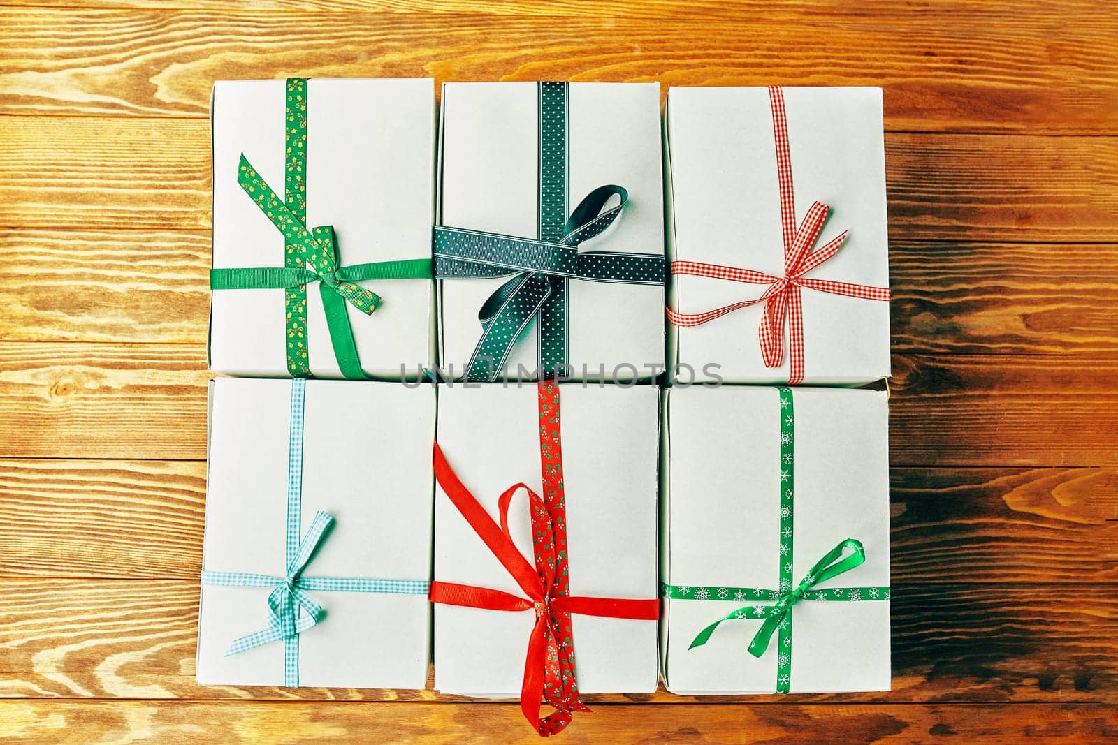 Stack of gift wrapped Christmas presents. A stack of gifts of white colors tied with different ribbons on a wooden background.