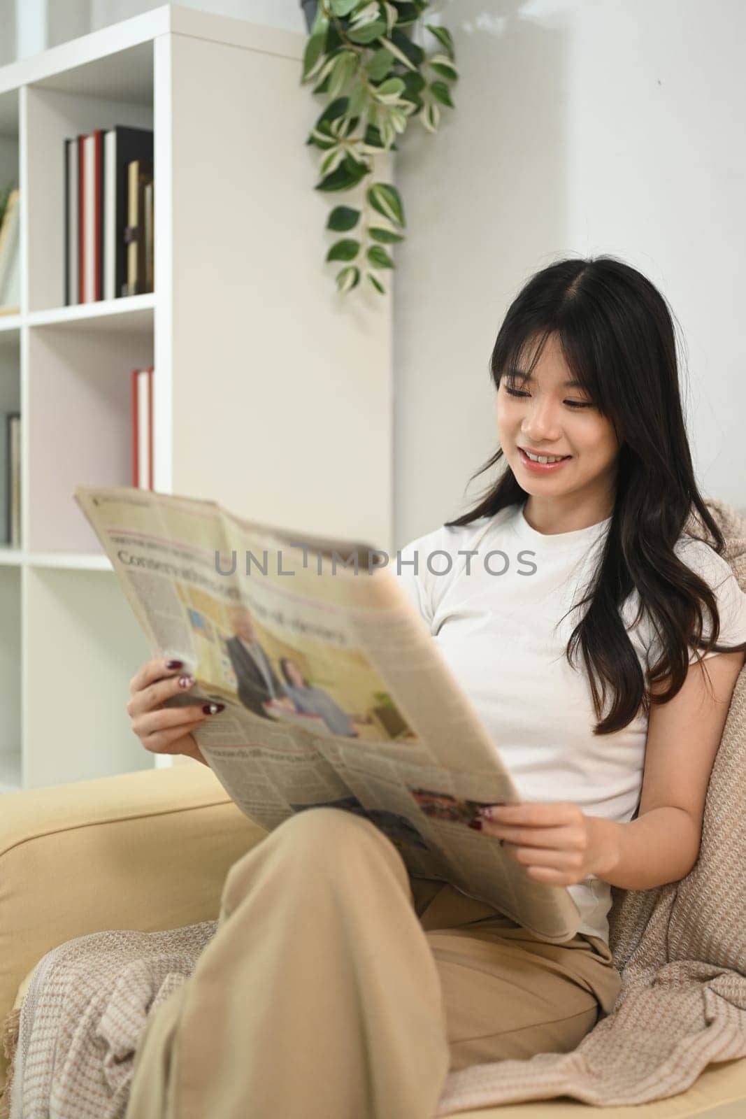 Relaxed young asian woman reading a newspaper in a living room.