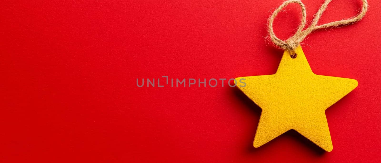 Bright yellow star ornament with a twine loop on a vibrant red background, featuring copy space for text.