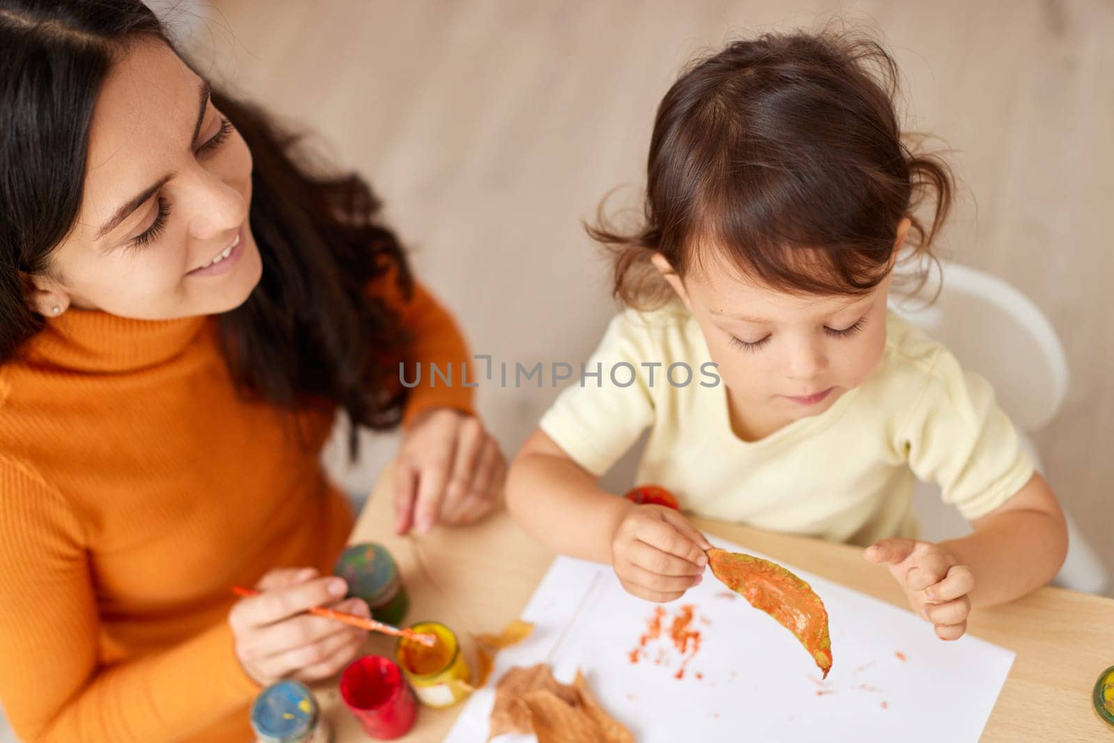happy little child girl and her mother drawing for the autumn holiday. Happy family making autumn decorations together